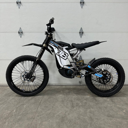 Sur-Ron Light Bee X electric motorcycle with white and black custom graphics kit, featuring geometric frame decals, fork guards, and battery housing wraps, displayed in a garage setting