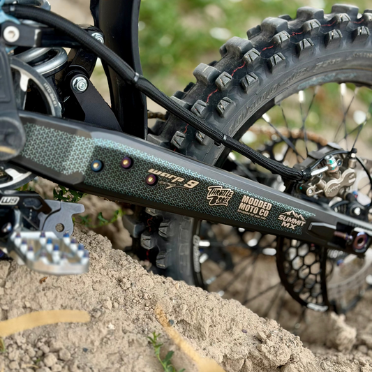 Close up image of a Technuc-Q EMX swing arm for the Surron Ultra Bee with a custom decal in a matte chrome finish.