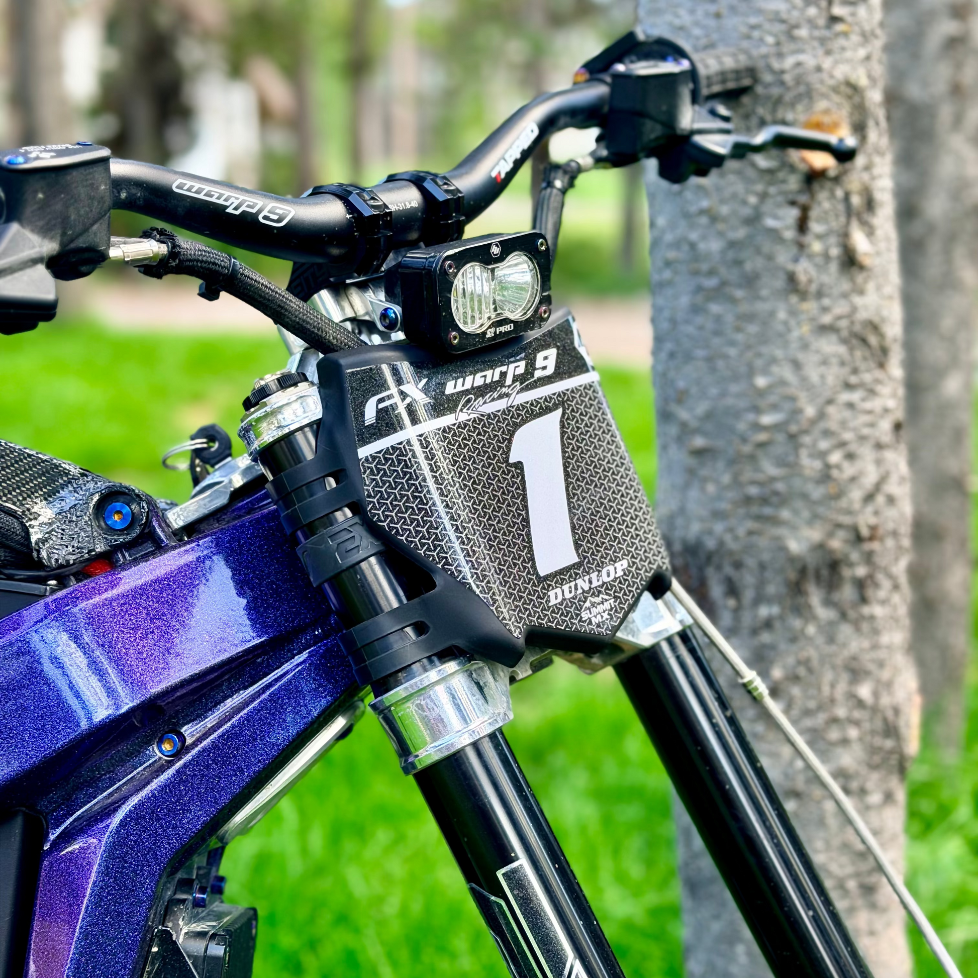 Close-up of a sparkly custom decal  on a motocutz number plate on a purple emoto bike with EXT suspension, warp 9 handle bars and a baja s2 pro headlight