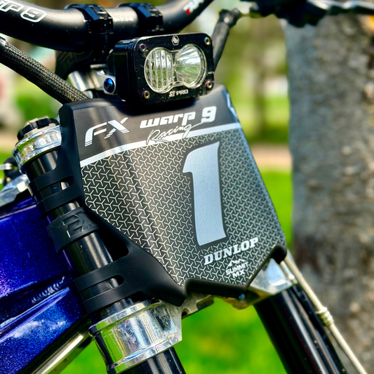 Close-up of a matte chrome custom decal  on a motocutz number plate on a purple emoto bike with EXT suspension, warp 9 handle bars and a baja s2 pro headlight